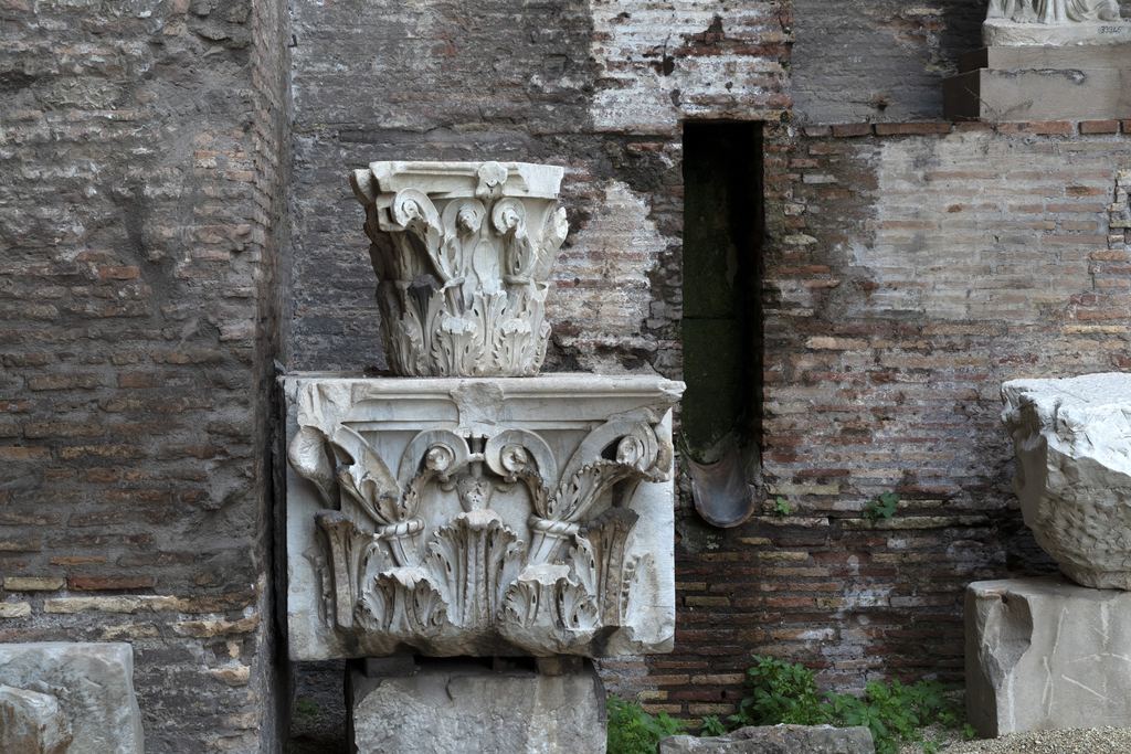 A carved marble Corinthian capital resting against Roman brickwork at the Baths of Diocletian in Rome