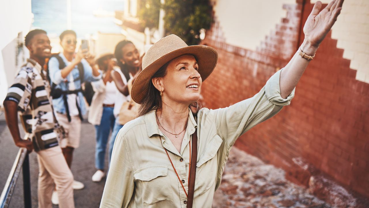 A guide raising an arm to point out a detail of old brickwork while a small group looks up