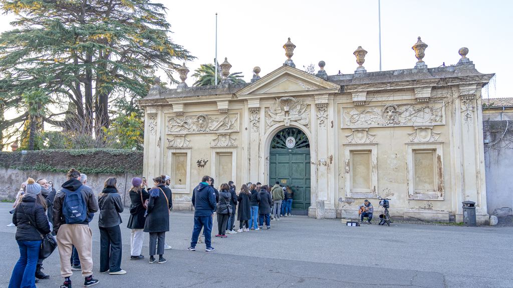 A line of visitors waiting along a barrier at the gate of a historic building