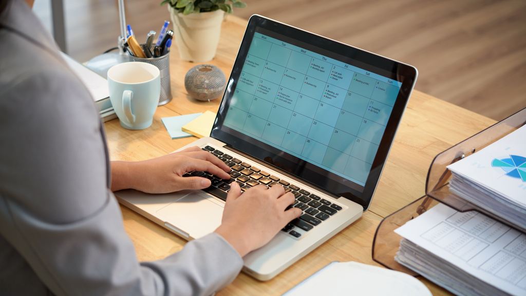 A person at a desk looking at a month calendar grid open on a laptop screen