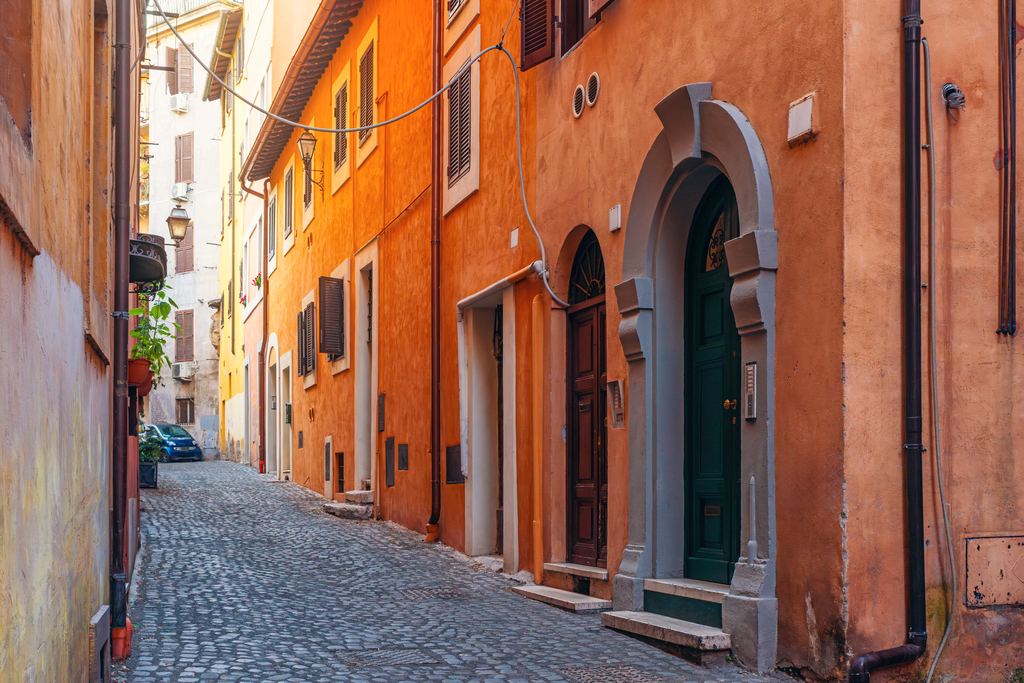 A narrow cobbled lane between terracotta buildings with wooden shutters and an arched doorway, empty