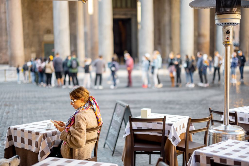 A woman at a cafe table in Piazza della Rotonda with the line of visitors and the Pantheon's columns behind her