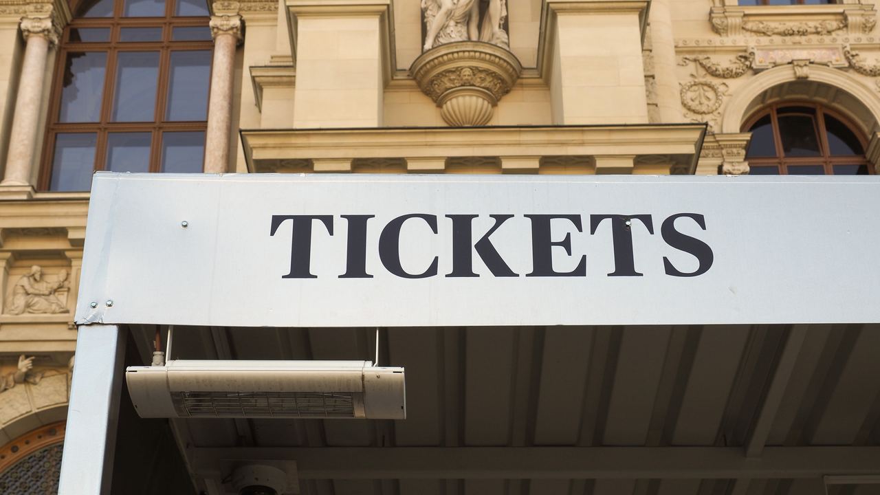 A pale stone sign reading TICKETS in capitals above a ticket booth set against a historic building
