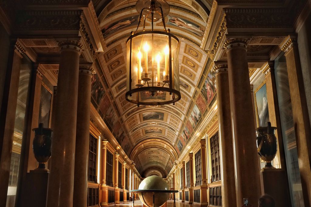 A long vaulted corridor with marble columns, a painted vault and a lit lantern hanging in the warm gloom