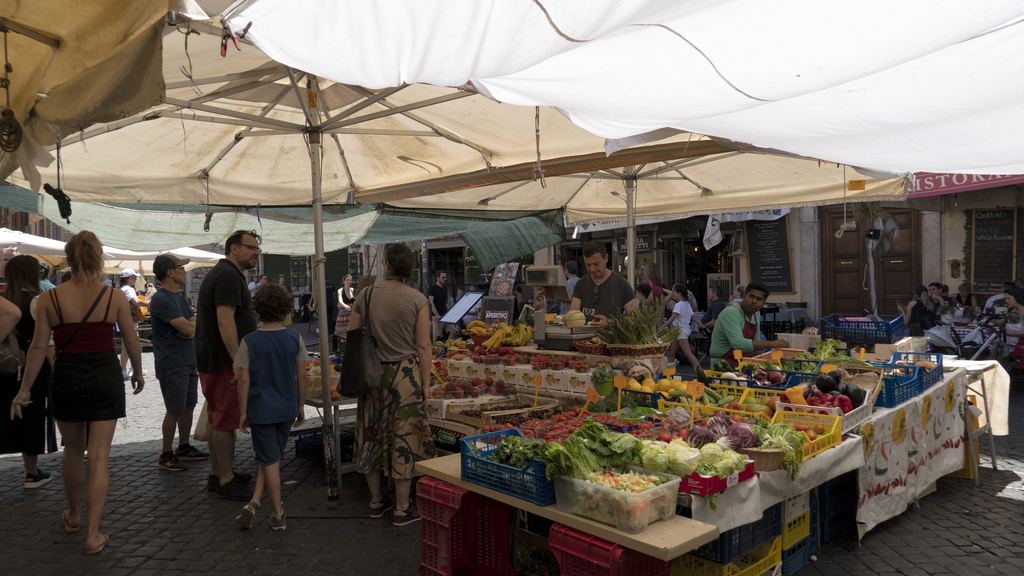 Market stalls under white awnings in Campo de' Fiori with shoppers on the cobbles