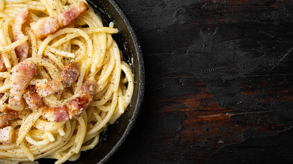 A cast iron pan of spaghetti alla carbonara with browned guanciale, seen from above