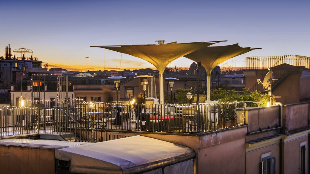 A roof terrace restaurant in Rome at sunset with the city's roofs and domes beyond