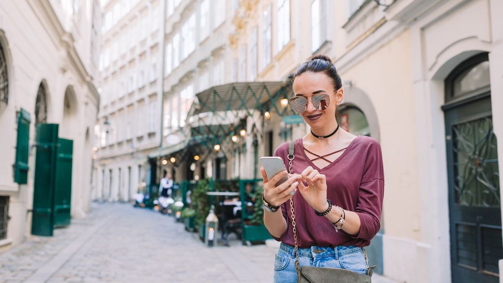 A traveller standing in an Italian street with green shutters, looking down at a phone screen