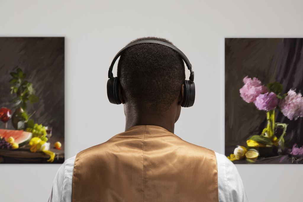 A visitor seen from behind wearing over-ear headphones, standing in front of a wall of pictures