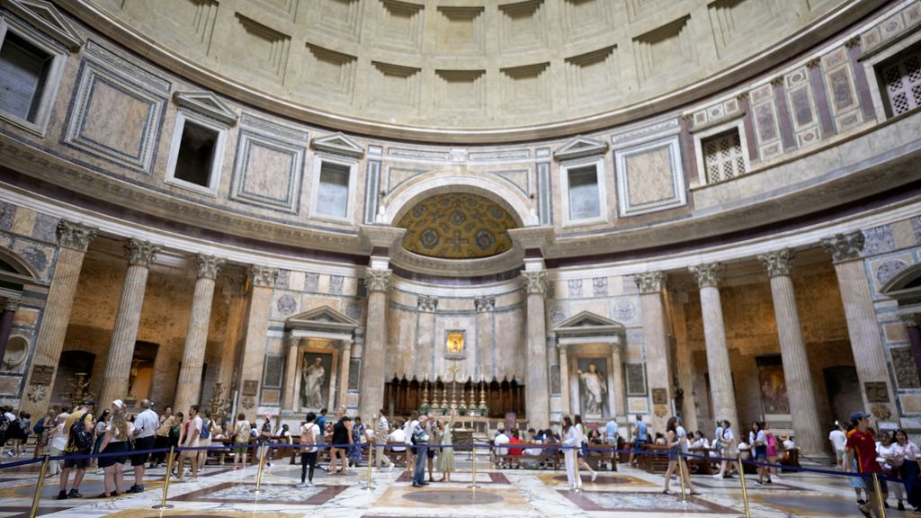 Visitors standing under the Pantheon's dome on the marble floor of the rotunda