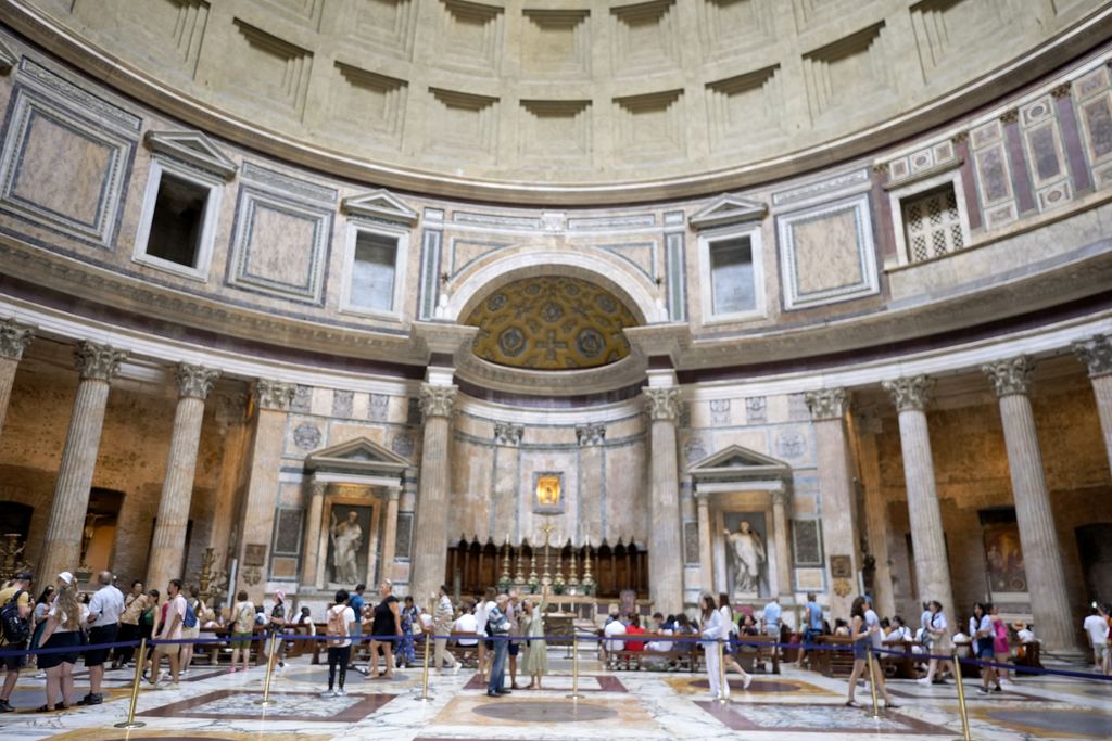 Visitors standing under the Pantheon's dome, spread across the marble floor of the single round room