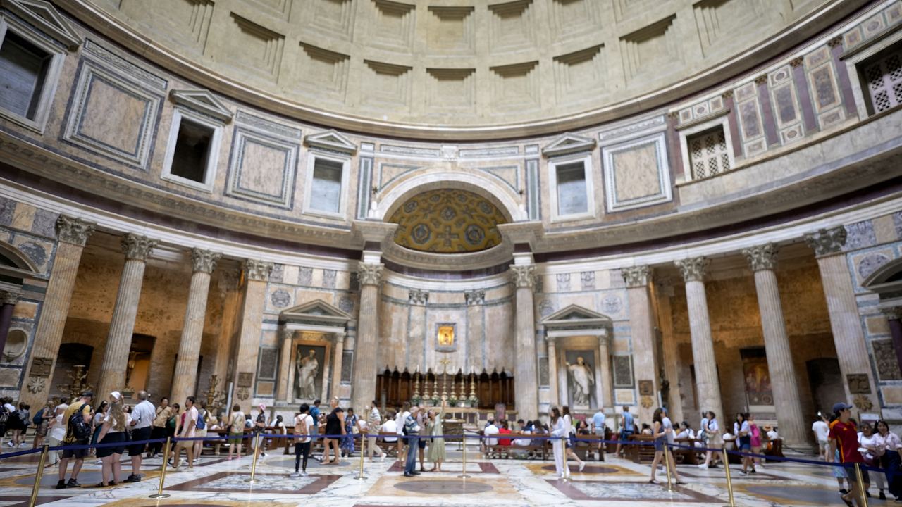 Visitors standing under the Pantheon's dome, spread across the marble floor of the single round room
