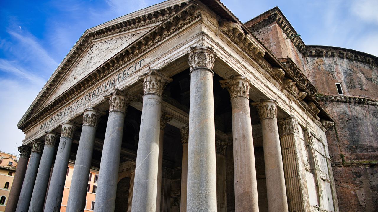 The Pantheon's portico in Rome seen from below, its granite columns and pediment inscription against a blue sky