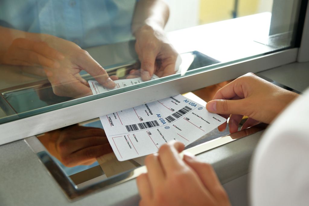 Hands passing a printed ticket through the slot of a box office window