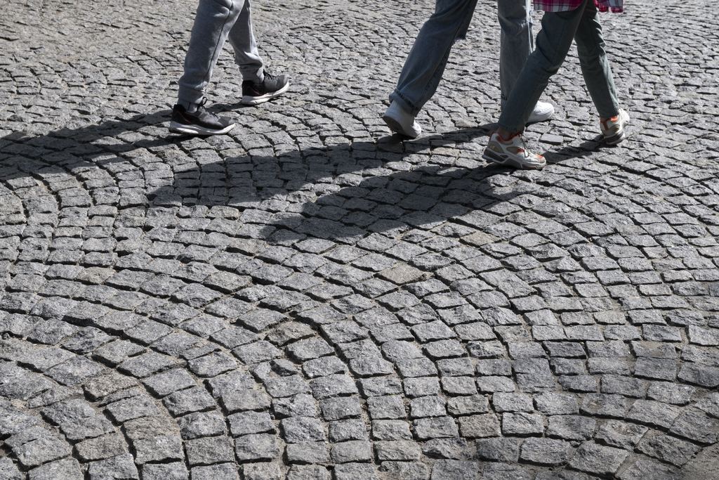 Close view of Rome's basalt sampietrini paving with two people walking across it in trainers