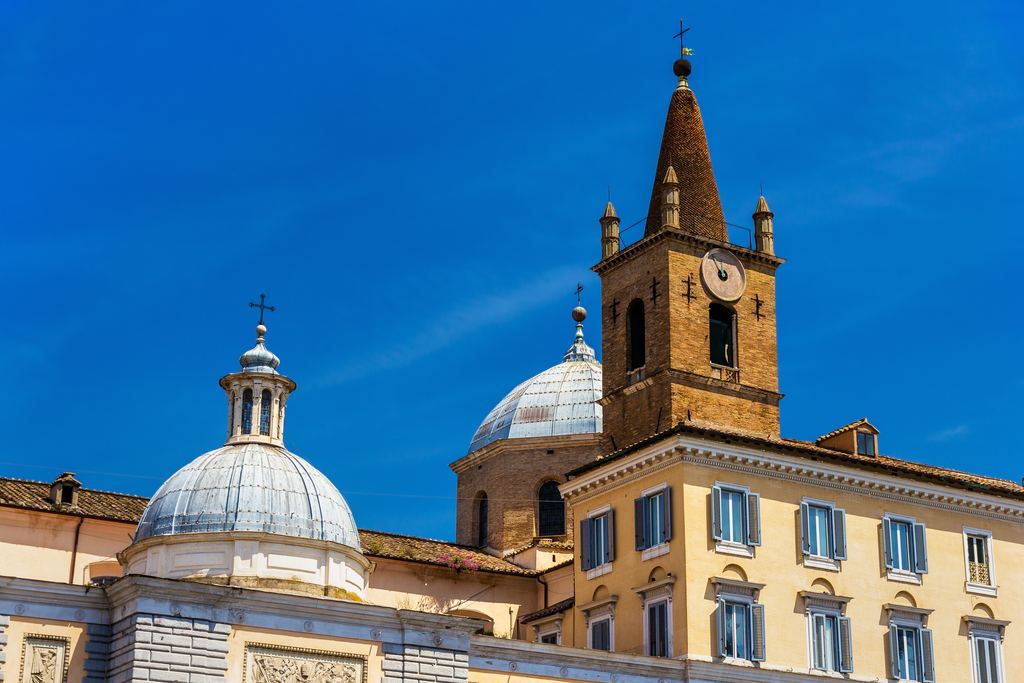 The dome and brick clock tower of the basilica of Santa Maria del Popolo in Rome seen from the square
