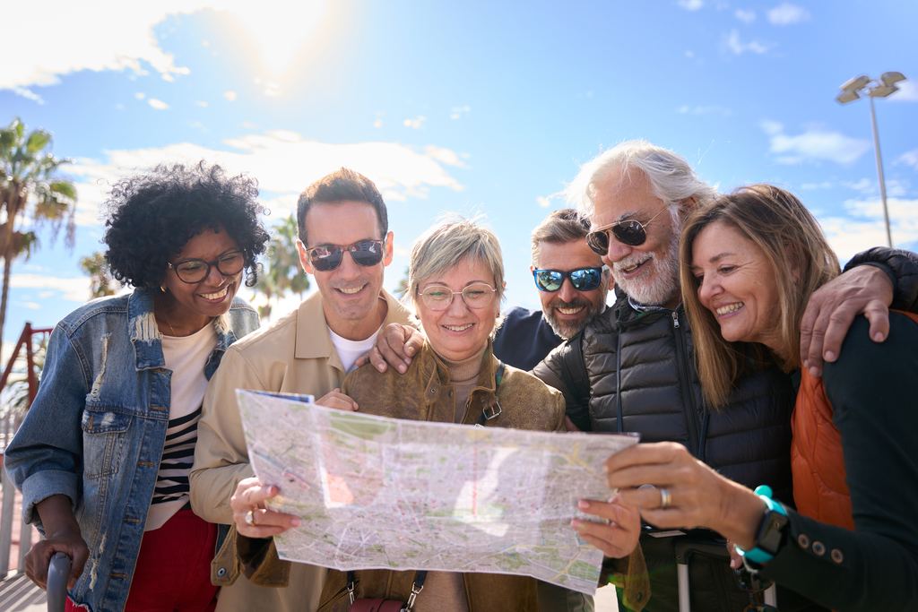 A group of six travellers standing together around an open paper map in bright daylight