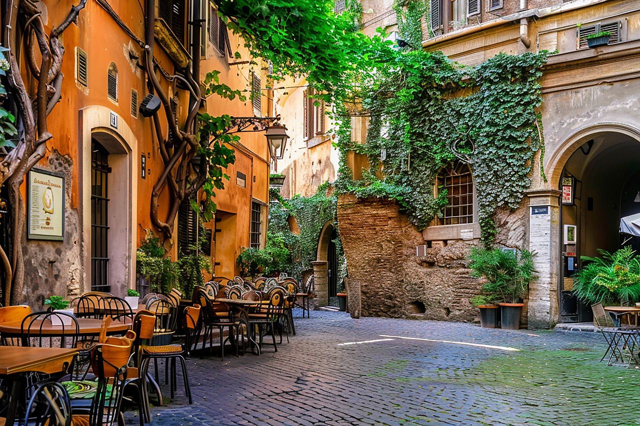 A Roman lane with an orange plastered wall, climbing greenery and a restaurant's tables and chairs set out under an awning