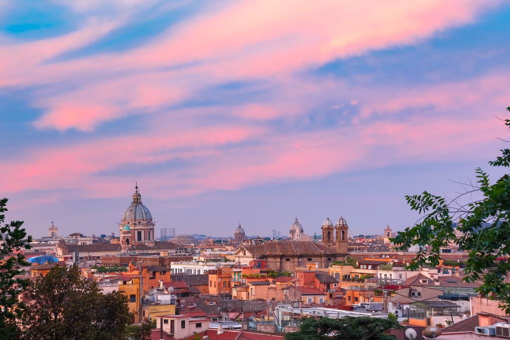 Rome's terracotta rooftops and church domes under an intense pink and magenta sunset sky