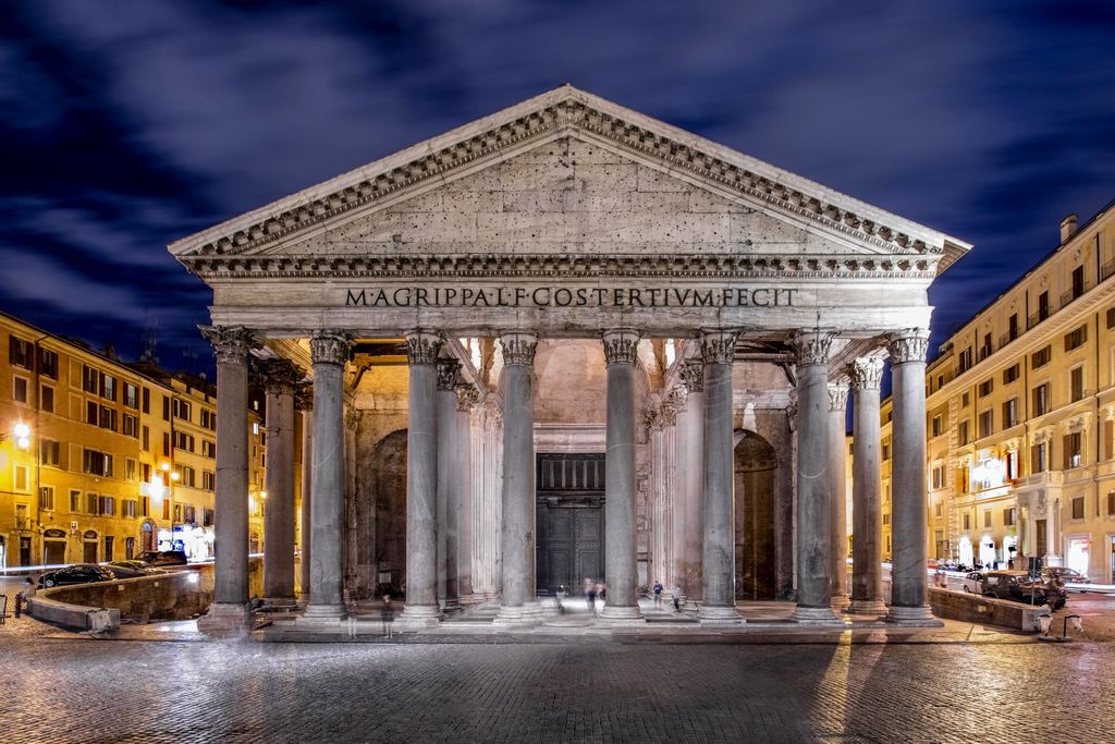 The Pantheon's facade floodlit at night under a deep blue sky, the square in front of it quiet