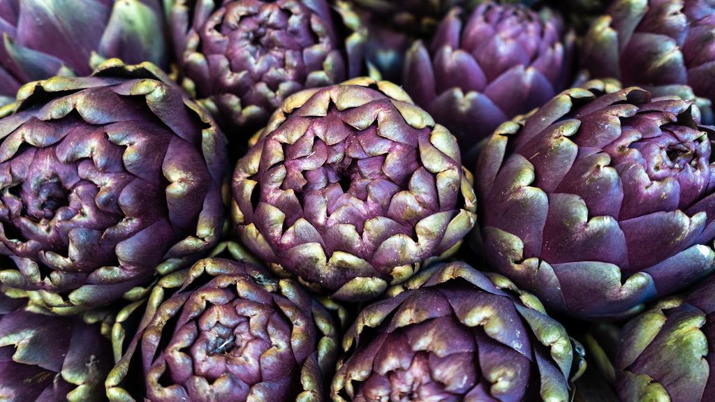 Purple Roman artichokes stacked tightly on a market stall