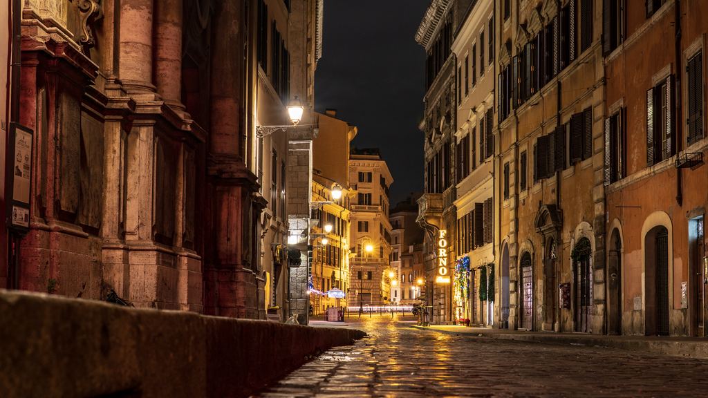A street in central Rome at night, wet paving reflecting the lamps, a church front on the left