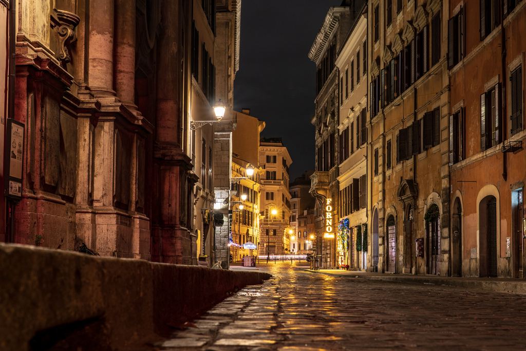 Via delle Quattro Fontane at night, wet paving reflecting the lamps and a church front on the left